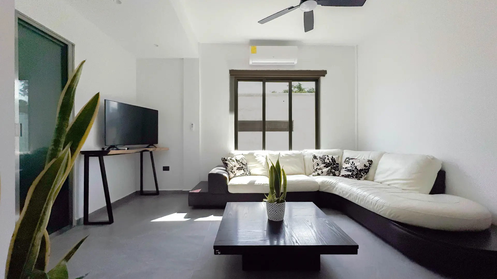 Sala con sofá en L claro, mesa de centro baja, televisión y ventilador de techo