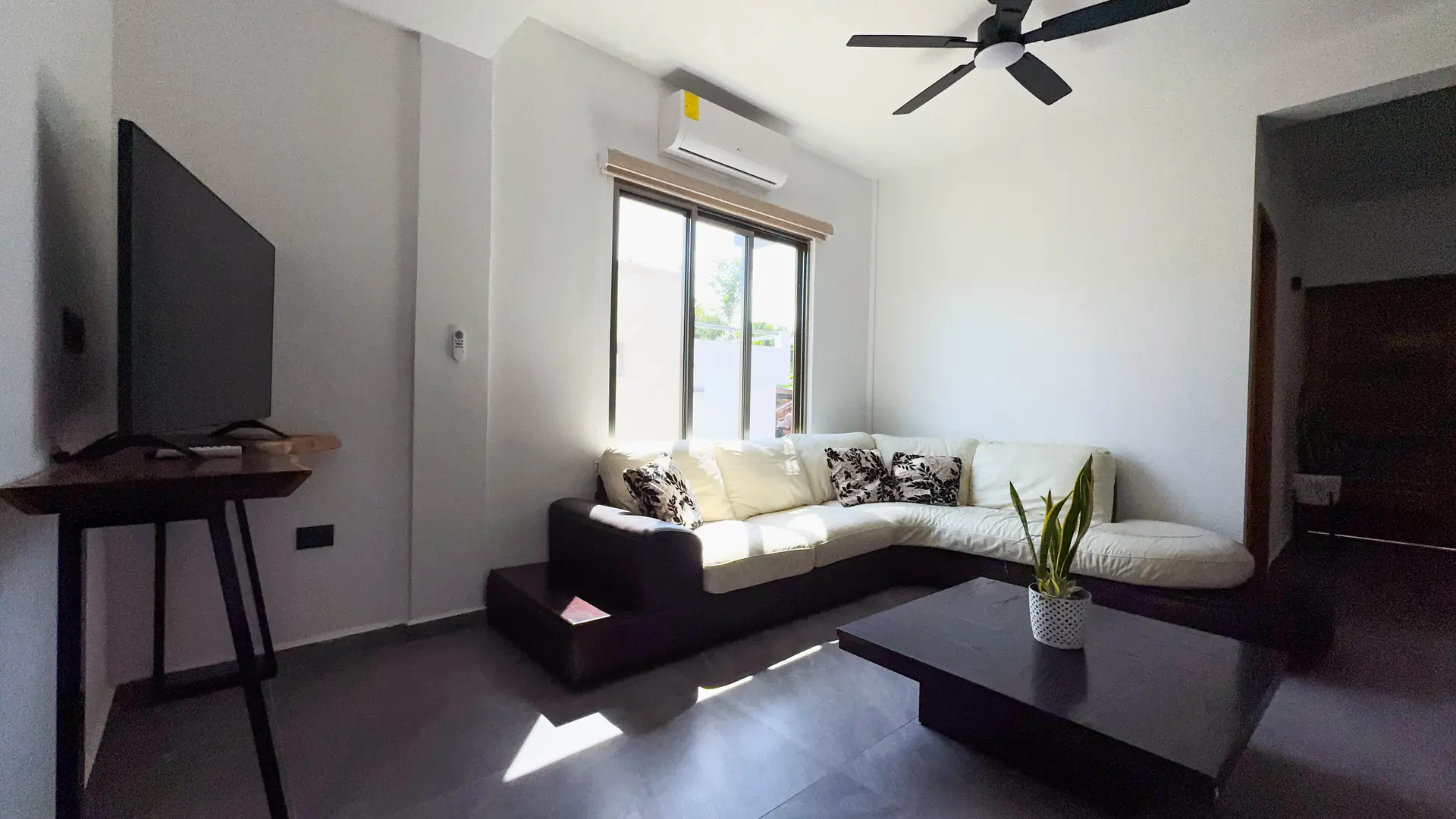 La sala desde la entrada, con la ventana, el aire acondicionado y el sofá en L