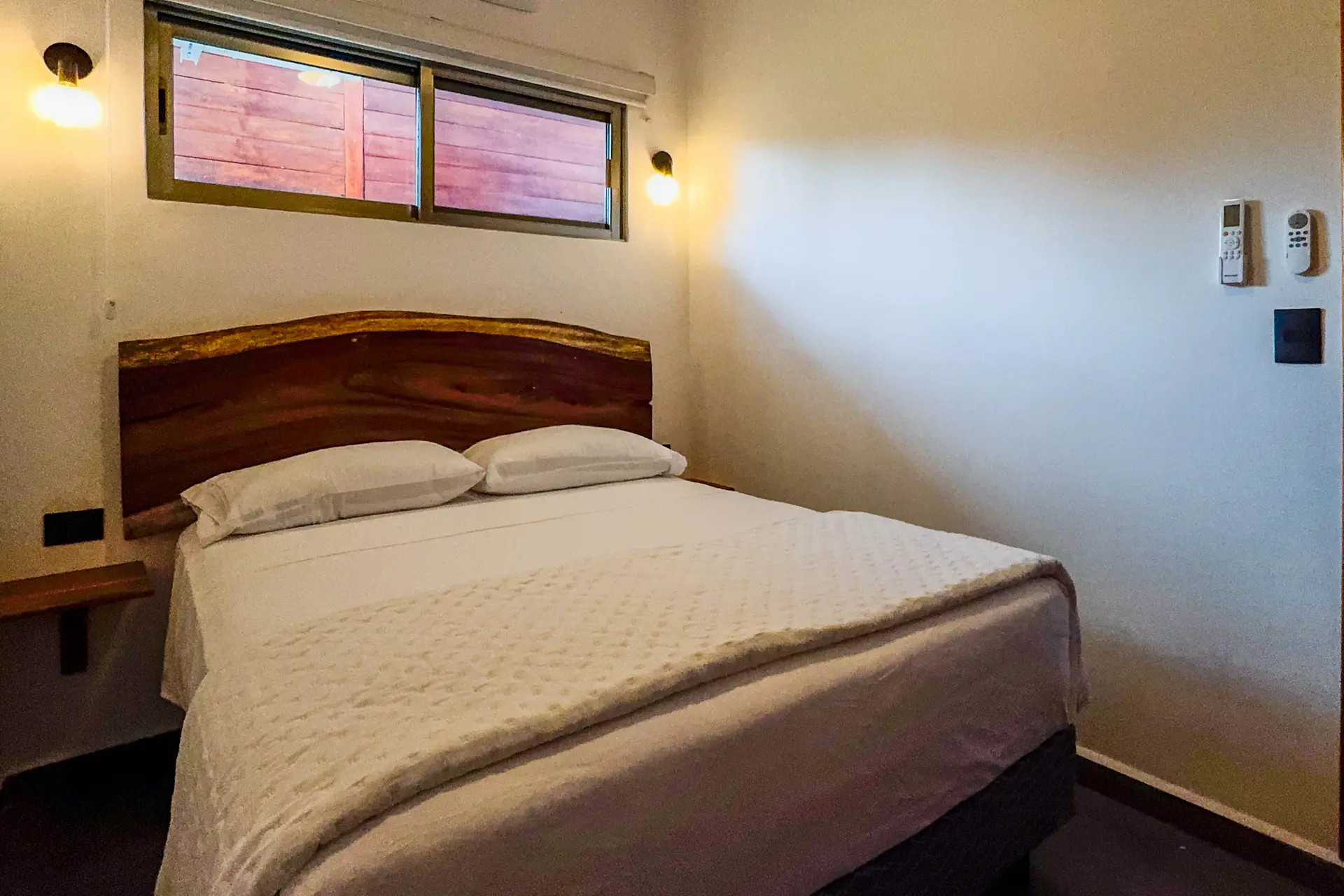 Recámara con cama matrimonial, cabecera de madera y una ventana alargada arriba