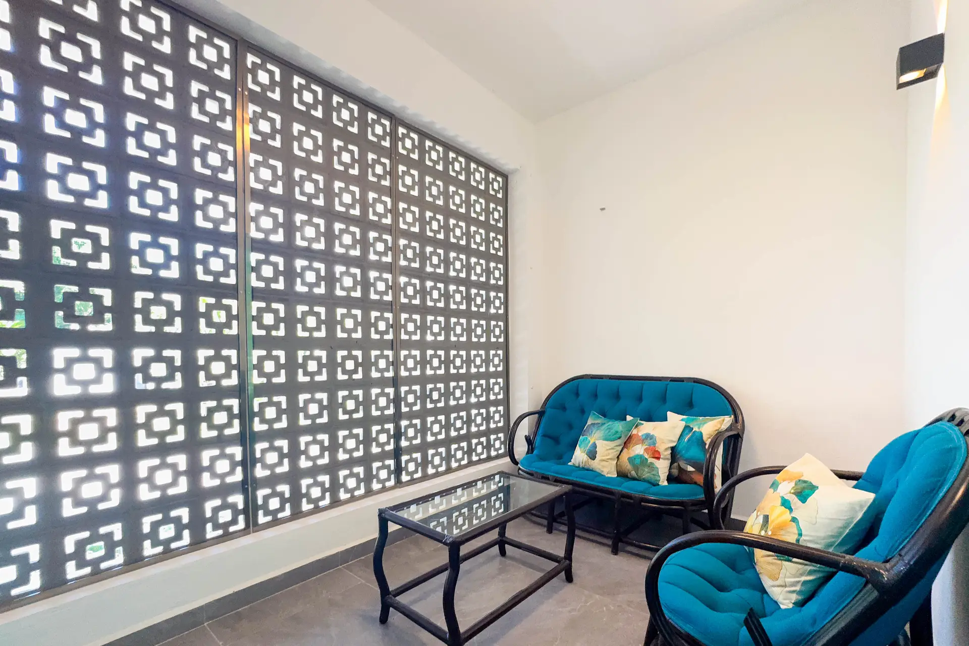 Estancia con dos sillones turquesa y mesa de cristal, junto a una celosía calada que filtra la luz