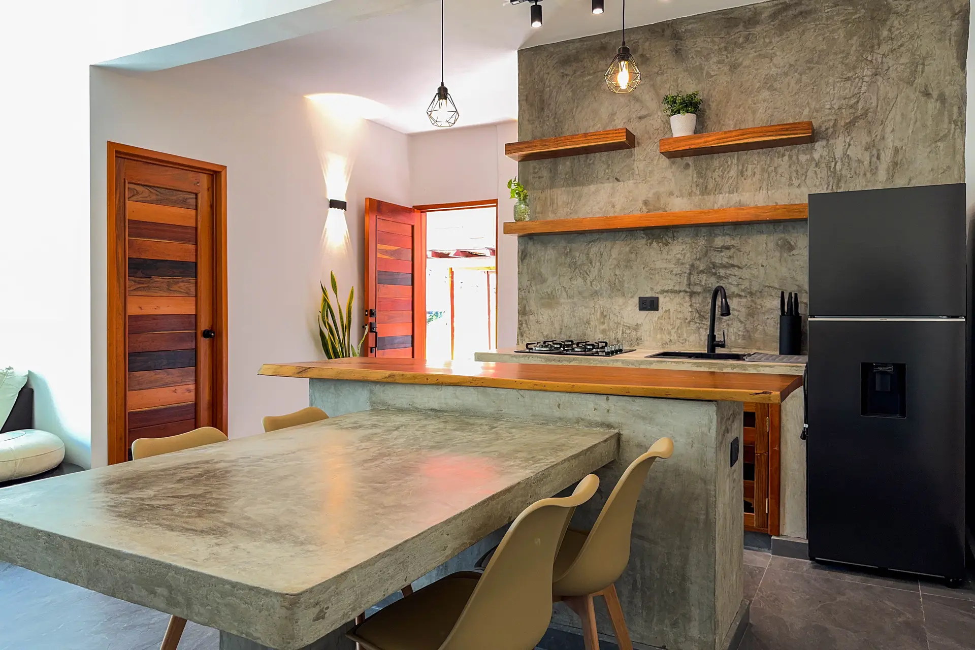 La cocina completa, con la barra, las repisas, el refrigerador y la puerta de madera al fondo
