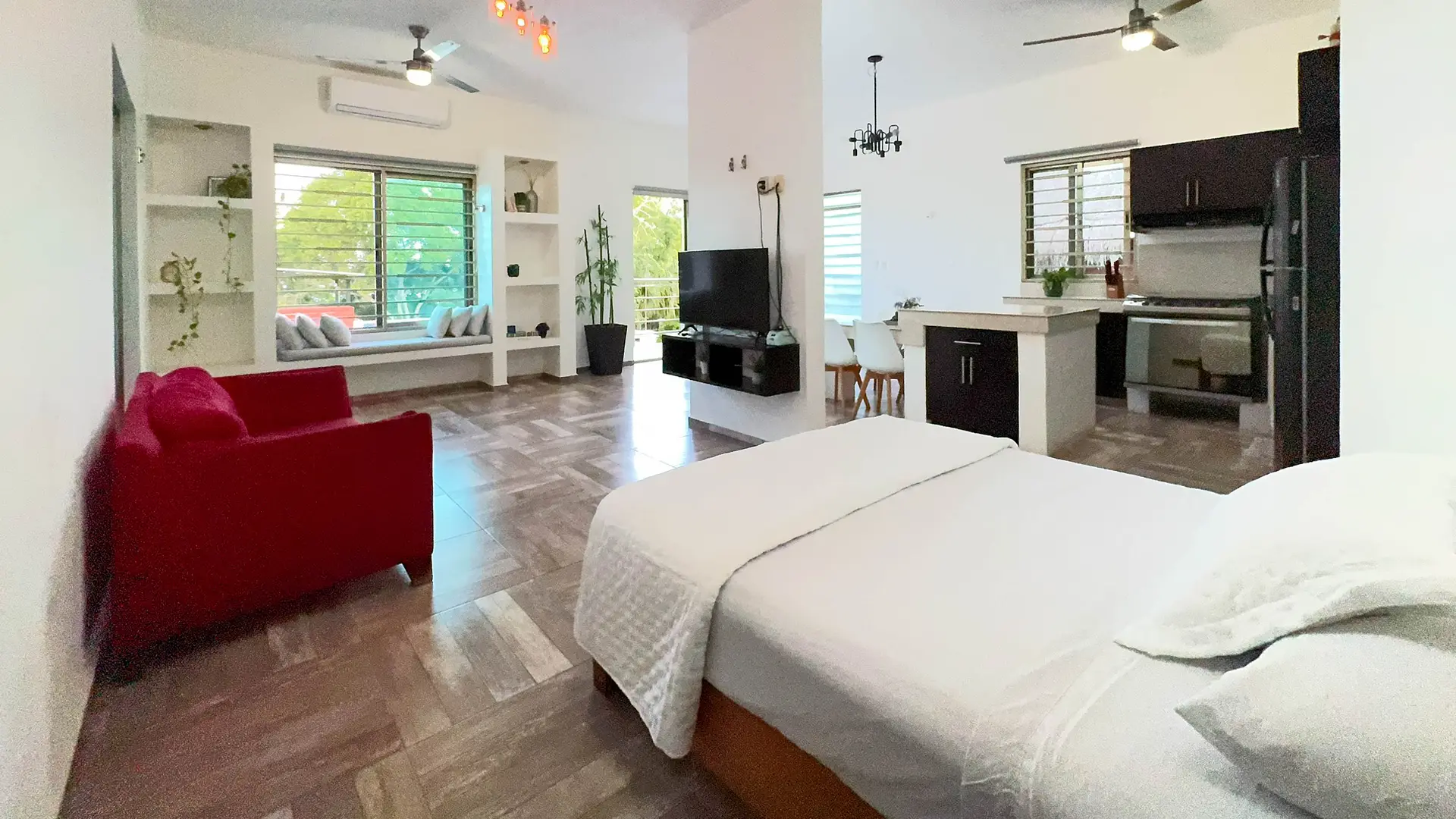 Estudio abierto con la cama en primer plano, un sofá rojo, la televisión y la cocina al fondo