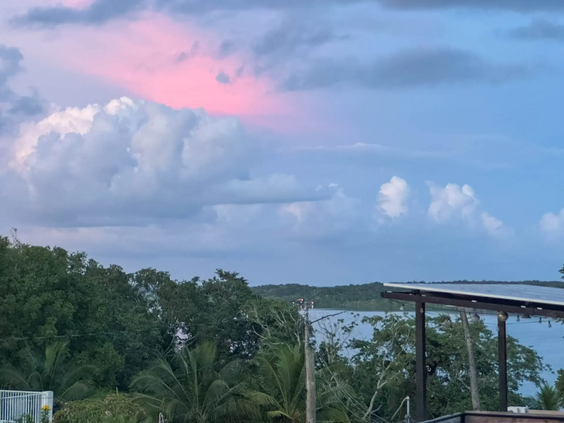Nubes rosadas sobre la laguna al atardecer, con la vegetación y una palapa en primer plano