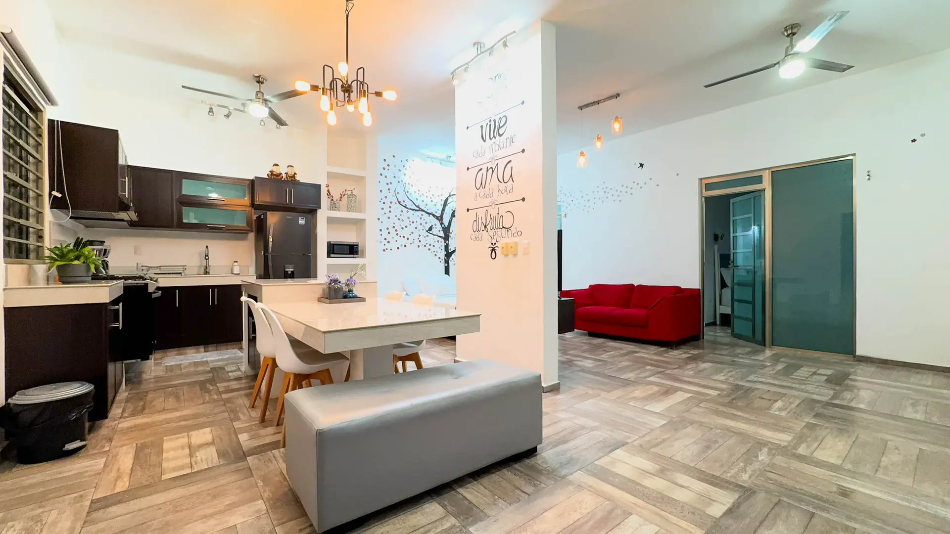 La estancia abierta, con la cocina, el comedor y el sofá rojo junto al mural de letras